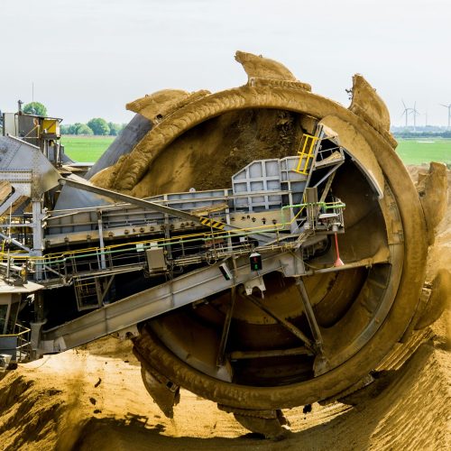 A large bucket wheel excavator working in an open pit mine against a green landscape.